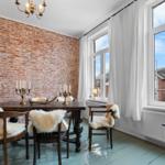 Esszimmer mit rustikalem Holztisch, Stühlen mit Fellkissen und Backsteinwand. Große Fenster mit weißen Vorhängen.