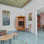 Wohnzimmer mit Holzschrank, Sofa und Gemälden. Durchgang zu Esszimmer mit Backsteinwand.