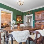 Esszimmer mit Holztisch, Stühlen mit Fell und antikem Schrank an grüner Wand.
