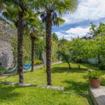 Garten mit Palmen, Schaukel und grünem Rasen. Steinmauer und Pflanzen im Hintergrund.