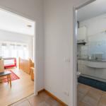 Zimmer mit Holzboden und Babybett. Nebenraum ist Bad mit Waschbecken und Spiegel.