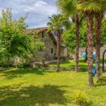 Steinhaus mit Garten, Palmen und Terrasse unter blauem Himmel.