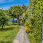 Pfad durch grünen Garten mit Palmen und blauem Pool. Wand mit Kletterpflanzen.