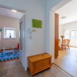 Eingangsbereich mit Holztruhe, Blick in Wohn- und Esszimmer mit Tisch, Stühlen und Fenstern.