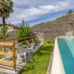 Poolbereich mit Liegestühlen und Tisch unter Palmen und Steinmauer.