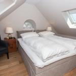 Schlafzimmer mit Dachschrägen, Doppelbett, Sessel und zwei Dachfenstern.