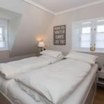 Schlafzimmer mit Doppelbett, zwei Fenstern und Nachttischen.