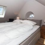 Schlafzimmer mit Dachschräge, Doppelbett, Fenster und Nachttisch mit Lampe.