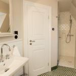 Badezimmer mit Dusche, Waschbecken und Spiegel. Fliesenboden und weiße Wände.