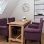 Esszimmer mit Holztisch, vier lila Stühlen, Bücherregal und Dachfenster.