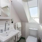 Badezimmer mit Waschbecken, Toilette und Dachfenster. Weiße Fliesen und Handtuchhalter.