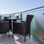 Terrasse mit Tisch und vier Stühlen, Glasgeländer und Blumenarrangement.