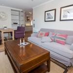 Wohnzimmer mit Sofa, Tisch und Stühlen. Wand mit Bildern und Uhr.