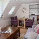 Wohnbereich mit Sofa, Tisch und Stühlen unter Dachschräge mit Fenster und Bücherregal.