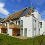 Moderne Villa mit Holzterrasse und grünem Garten unter blauem Himmel.