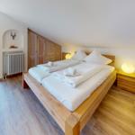 Schlafzimmer mit Holzbett, Nachttisch und Fenster. Holzschrank und Heizkörper sind sichtbar.