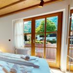 Schlafzimmer mit Blick auf grüne Landschaft und Balkon. Holzdecke und weißes Bett.