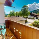 Terrasse mit zwei grünen Stühlen und Holzgeländer. Blick auf Haus und grüne Berge.