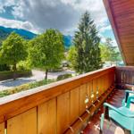 Terrasse mit Holzgeländer und zwei grünen Stühlen. Blick auf Straße, Bäume und Berge.