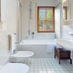 Badezimmer mit Badewanne, Dusche, Waschbecken und Toilette. Holzfenster mit Jalousie.