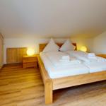 Schlafzimmer mit Holzbett, Nachttisch und Kleiderschrank. Holzfußboden und Dachschrägen.