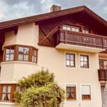Ein zweistöckiges Haus mit Balkonen und Fenstern. Im Hintergrund sind Berge zu sehen.