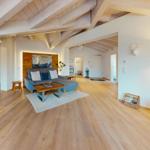 Wohn- und Küchenbereich mit Holzboden, Sofa und TV. Deckenbalken und Wanddekoration sichtbar.