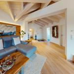 Wohnbereich mit Holzdecke, Sofa und Holzboden. Wandbild und Hirschgeweih dekorieren den Raum.