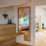 Durchgang mit Spiegel zeigt Schlafzimmer mit Bett und Balkon. Holzdecke und Boden.