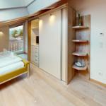 Schlafzimmer mit Bett, Kleiderschrank und Balkonansicht.