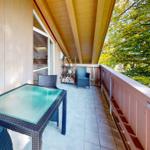 Terrasse mit Tisch, Stühlen und Blick auf Bäume. Holzverkleidung und Grillplatz.