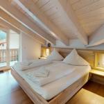 Doppelbett mit Blick auf Balkon und Wald. Holzdecke und Boden.