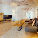 Wohnzimmer mit Holzboden, Sofa, Couchtisch und Fernseher unter Holzbalkendecke.