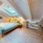 Doppelzimmer mit Dachschrägen, Bett, Schreibtisch und Dachfenster.