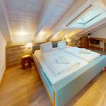 Doppelbettzimmer mit Holzdecke, Dachfenster und Schreibtisch.