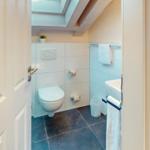 Badezimmer mit Toilette, Waschbecken und Dachfenster. Holzbalken und weiße Fliesen.