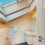 Badezimmer mit Dachfenster, Waschbecken und Toilette. Holzdecke und Fliesenboden.