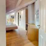 Schlafzimmer mit Holzboden, Bett, Schrank und Schreibtisch. Dachboden mit Holzdecke und Fenster.