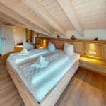 Schlafzimmer mit Holzbett, Deckenbalken und Schreibtisch mit Stuhl.