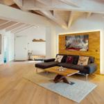 Wohnzimmer mit Holzboden, Sofa und Tisch. Deckenbalken und Wandbild sichtbar.