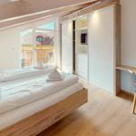 Schlafzimmer mit Doppelbett, Schwebetüren-Schrank und Schreibtisch mit Stuhl.
