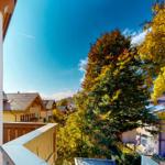 Blick vom Balkon auf einen Dorfplatz mit Bäumen im Herbst.