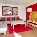Wohnzimmer mit grauem Sofa, rotem Teppich und Holzmöbeln. Wandbild zeigt Berge.