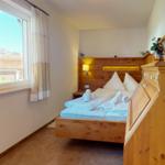 Schlafzimmer mit Holzbett, Fenster und Schrank. Blick auf Dach und Bäume.