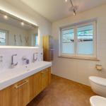 Badezimmer mit Waschtisch, Spiegel, Toilette und Fenster.