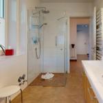 Badezimmer mit Dusche, Waschbecken und Fenster mit Pflanze.