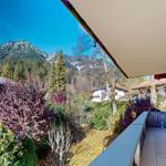 Terrasse mit Blick auf bewaldete Berge und umliegende Häuser.
