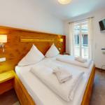 Schlafzimmer mit Bett, Holzwand, TV und Fenster zur Terrasse.