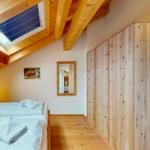 Schlafzimmer mit Dachschrägen, Holzboden und Dachfenster. Holzwand und Spiegel an der Wand.