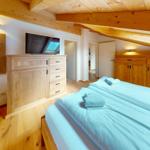 Schlafzimmer mit Holzboden, Bett, Kleiderschrank und Fernseher unter Holzdecke.